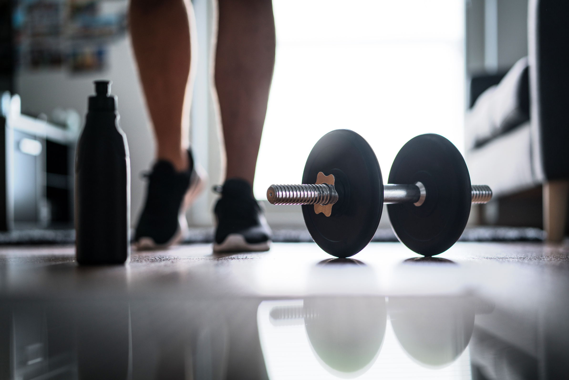 Fitness, home workout and weight training concept. Man starting to exercise with dumbbell. Water or protein shake bottle.